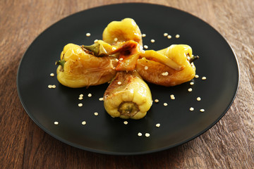 Black plate with roasted peppers on wooden background