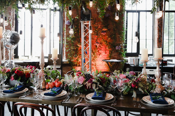 Dinner table stands in loft decorated with flower and greenery g