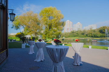 Bar tables with little red bouquets stand on the backyard with a