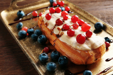 Tasty eclair with berries on tray and wooden background
