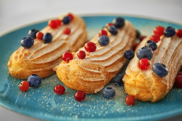 Tasty eclairs with berries on blue plate