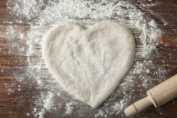 Pizza dough in heart shape with flour on table