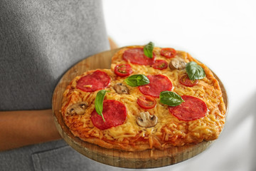 Woman holding tasty pizza on wooden tray