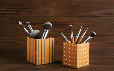 Set of makeup brushes in decorative boxes on wooden background