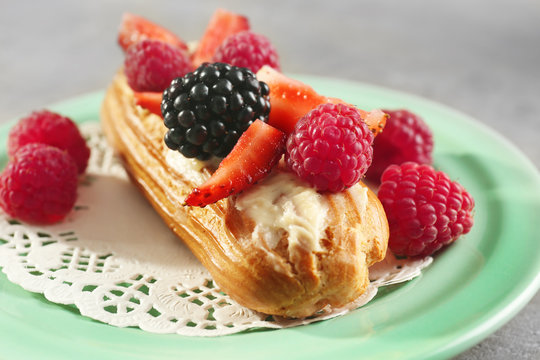 Green plate with delicious eclair, berries and doily, close up