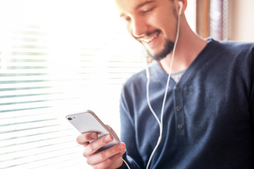 Happy man listening to music on smartphone in bright home interior