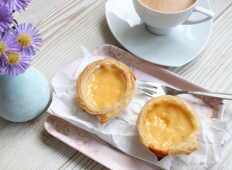 Pasteis de Nata - kleine portugiesische Pudding-Törtchen mit Kaffee und Blumen auf einem grauen Holztisch