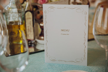Card with menu in golden design stands between empty glassware