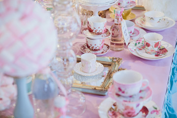 Little tea cups stand on the mirror on a pink dinner table