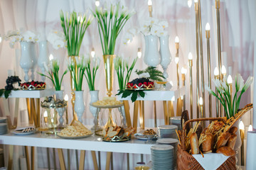 Basket with bread stands behind white buffet full of cheese