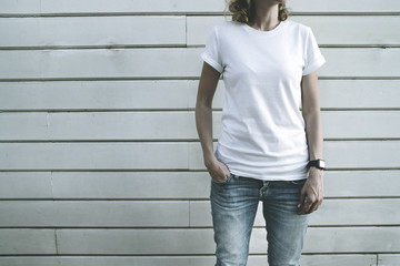 Front view. Girl in a white T-shirt and blue faded jeans standing with her hand in her pocket, on...