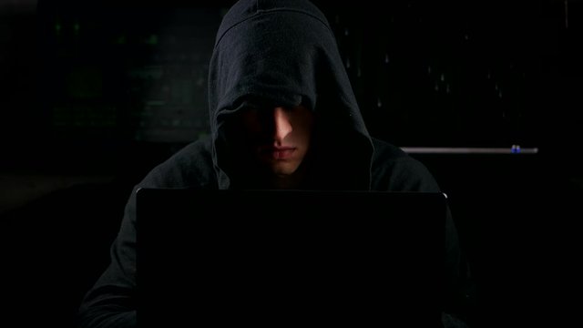 mysterious hacker in a mantle working on a computer in a dark office room