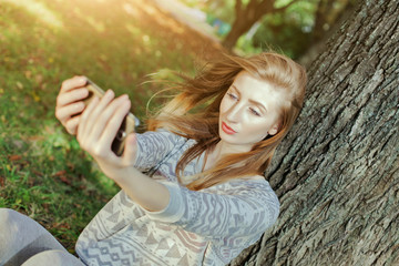 Naklejka premium Beautiful girl with blue eyes makes selfie outdoors next to the tree and the house