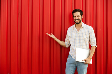 man presenting one side with laptop in hands on red background