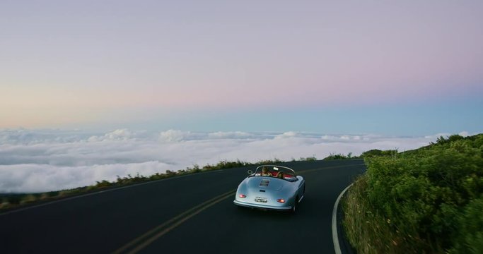 Happy couple driving on country road in classic vintage sports car, summer road trip freedom concept