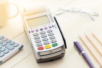 Credit Card Terminal or EDC on cashier wooden table in the store with calculator, pen, pencil, digital tablet and glasses on wooden background with copy space.
