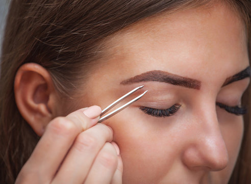 Master makeup corrects and gives shape to pull out with forceps previously painted with henna eyebrows in a beauty salon. Professional care for face