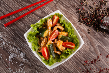 Spicy salad with chili cucumbers in a white plate on a wooden ba