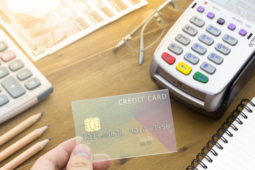 Cashier hand holding a Credit card over EDC machine or credit card terminal with calculator and glasses. A credit card over japanese bank notes.