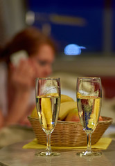 Two glasses of sparkling wine in hotel room with woman in backgr