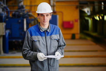 A man in overalls and a helmet stands near a kiln and holding a brick