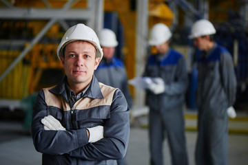 A man in overalls and a helmet stands near a kiln and holding a brick