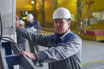 A man in overalls and a helmet stands near a kiln and holding a brick