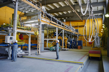 A man in overalls and a helmet stands near a kiln and holding a brick