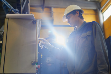 A man in overalls and a helmet stands near a kiln and holding a brick