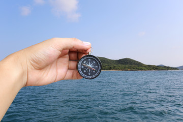 Hand of man holding a compass and sea island view.