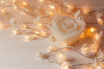 Burning lights and candle rose on white wooden background. Christmas background.