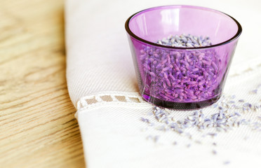 Dried lavender flowers in a purple glass on fabric and wood. Lavandula angustifolia with pale purple flowers used as culinary herbs and for essential oil extractions. Isolated macro photo close up.