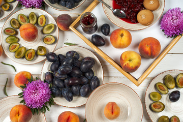 Colorful fruit set of purple, red and orange background in bowls. Plum, peaches, watermelon sliced above white tabletop