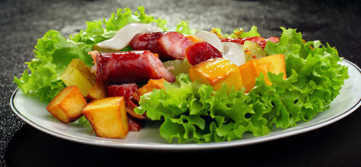 Salad.Chorizo sausage, lettuce, pickled cucumber fried potato with mayonnaise.Dark background