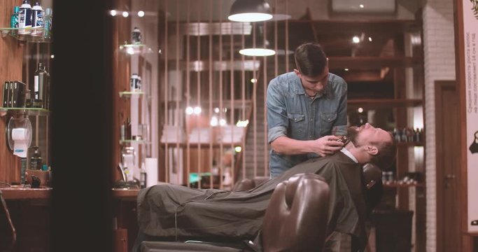 Hairdressing process at barbershop 4k video. Barber cutting beard with clipper of client man lumberjack