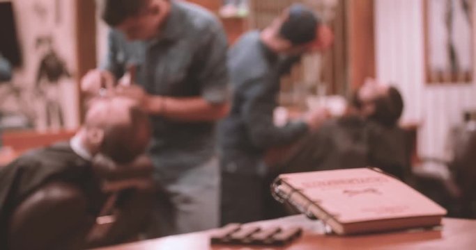 Hairdressing process at vintage lumberjack barbershop 4k bokeh video. Barbers working with client: cutting man's beards with clipper, retro notepad book