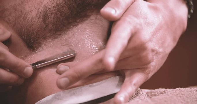 Barber hand shave beard with straight razor 4k video in barbershop. Extremely close-up view of client man neck