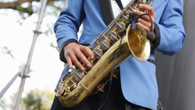 Musician playing saxophone close-up. Wireless microphone saxophone. Man fingers pressing keys of the musical instrument. Saxophonist in blue suit playing on golden saxophone. Swing, jazz, blues music.