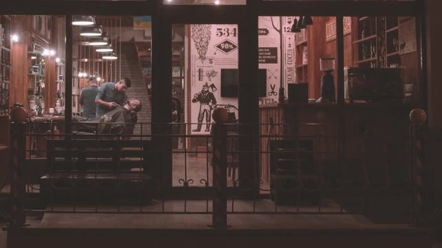 Vintage Barbershop Exterior HD Video. Barber Working With Client Beard. View From Street Through Panoramic Glass Window Entrance To Retro Hairdressing Salon Interior