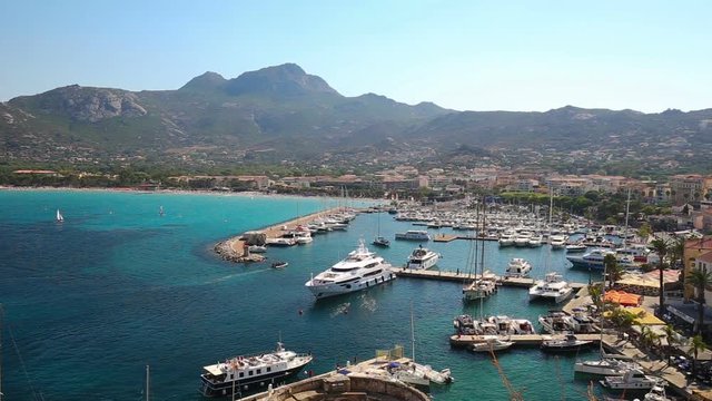View to Calvi beach, historic houses in Calvi old town with turquoise clear ocean water in harbor with boats and yachts, Corsica, France, Europe