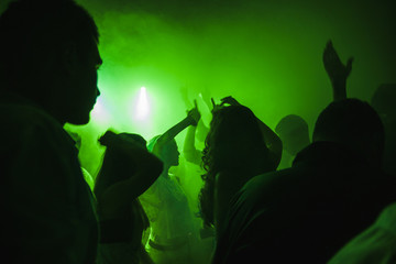 Serata in discoteca con gente che balla con le mani alzate dietro a neo e led verdi e nebbia.