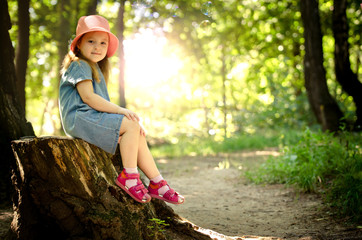 Little girl in a pink hat sitting on a tree stump - 123148967