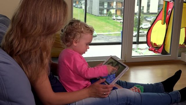 Small girl and her mother watching family photos on tablet computer screen