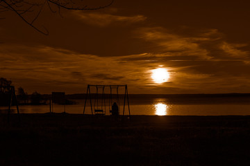 The girl on a cold autumn decline sits alone on a swing