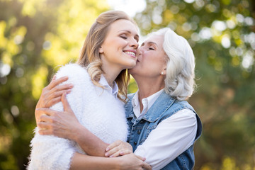 Beautiful gray haired woman kissing her daughter in the cheek.