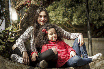 Niña y adolescente, hermanas felices sentadas juntas en el parque.