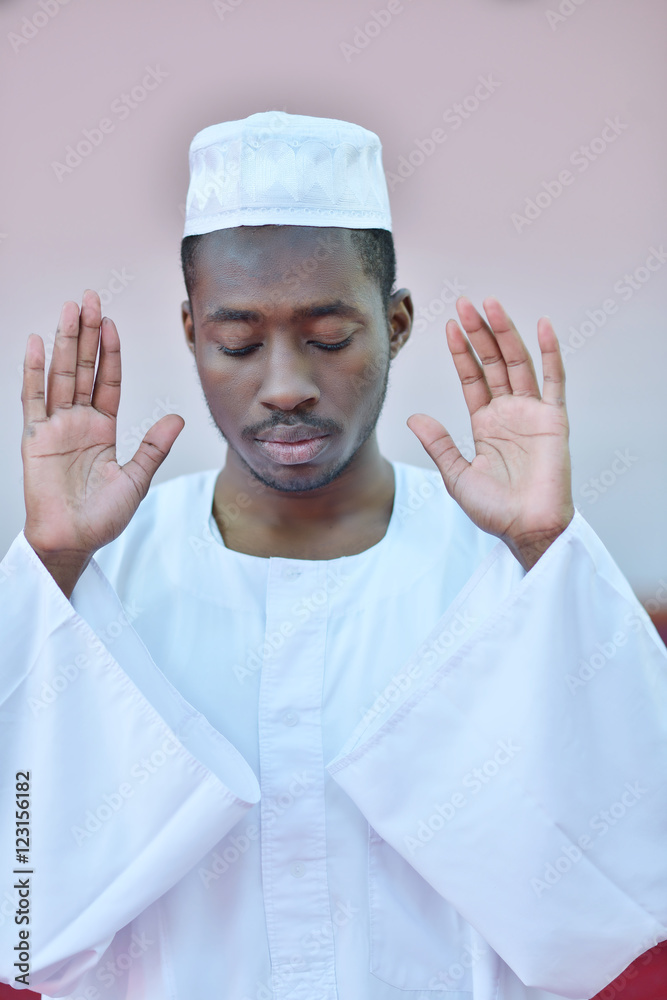 Wall mural African Muslim Man Making Traditional Prayer To God While Wearing A Traditional Cap Dishdasha