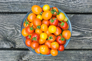 Fototapeta na wymiar Flat view from above of red and yellow cherry tomatoes in glass bowl against rustic wooden background