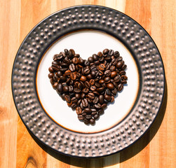 Roasted coffee beans in shape of a heart displayed on a decorative plate.