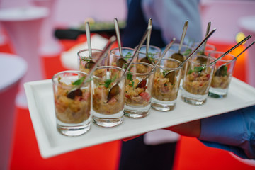 Waiter carries square dish with shots full of snacks